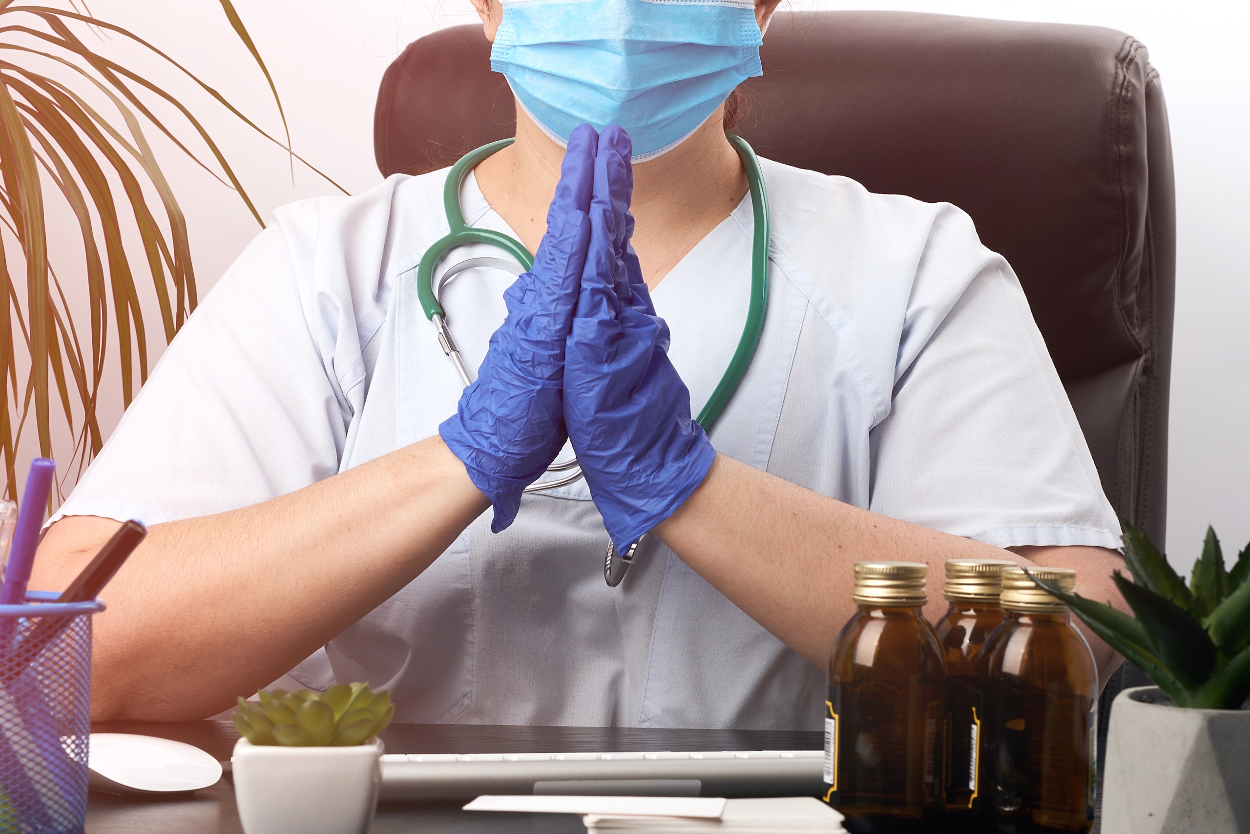 Ärztin mit Maske und Handschuhen am Schreibtisch